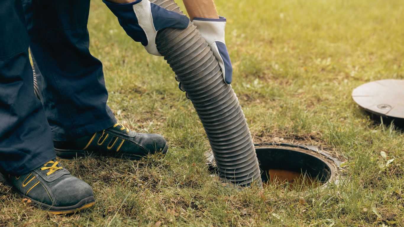 Worker using a large hose to clean a sewage system, addressing sewage damage.