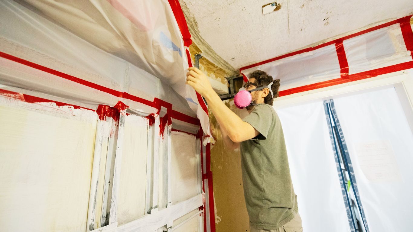 A professional in safety gear seals off a contaminated area during cleanup, representing the importance of accessible mold remediation financing for safe home recovery.
