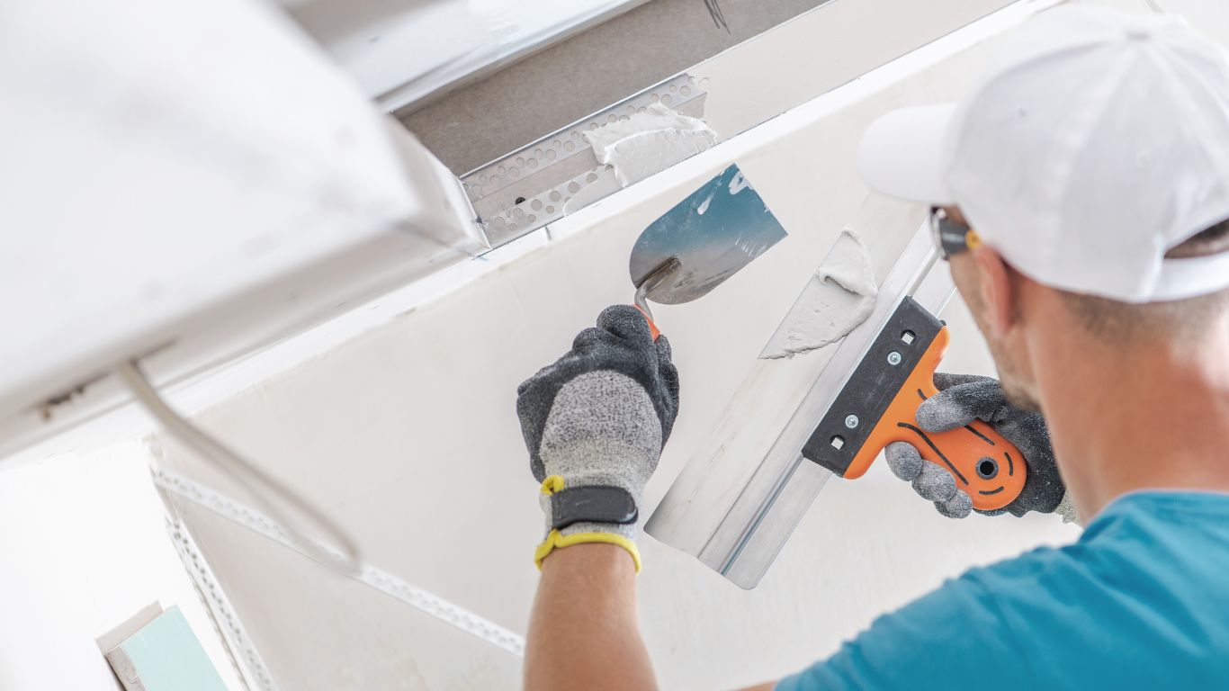 Worker repairing ceiling with tools during drywall & interior painting makeover.