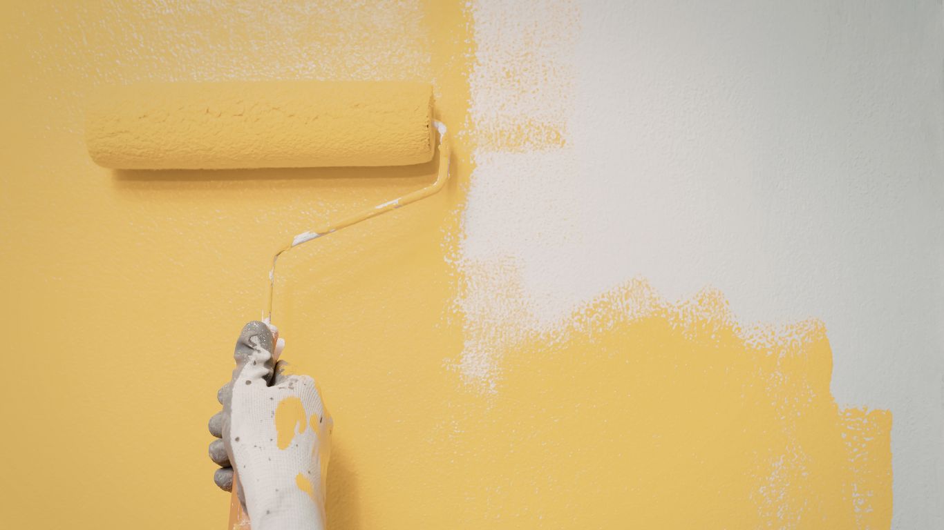 A person rolling yellow paint on a wall, showcasing expert interior painting skills.